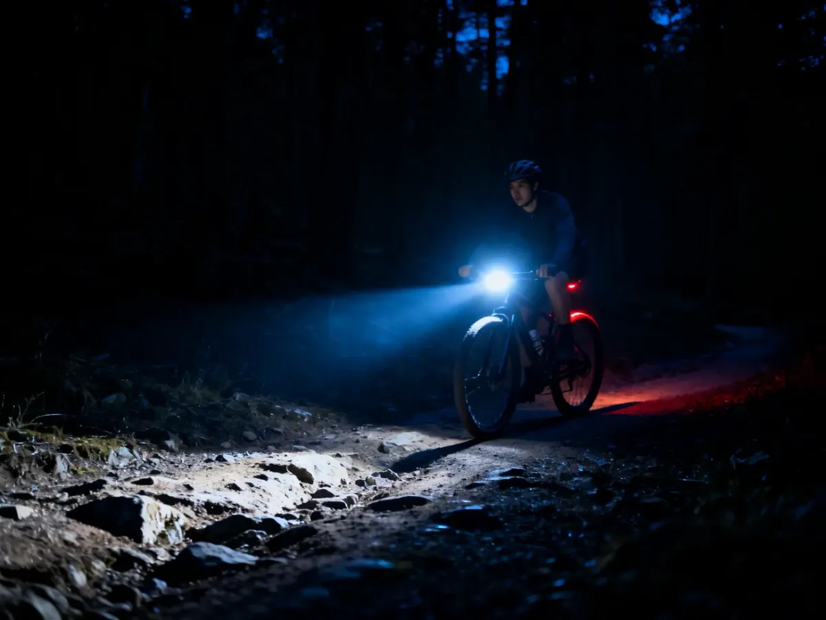 Rowerzysta oświetlający mocną lampką ciemny leśny szlak